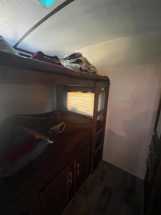 **RV rental** bunk beds with blankets, window with blinds, and lower storage cabinets. Cozy camper interior view.. Keystone RV Cougar 2019
