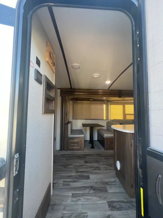This inviting rv rental interior, seen from the open door, features a modern dinette, counter, and sleek wood-look flooring.. Keystone RV Cougar 2019