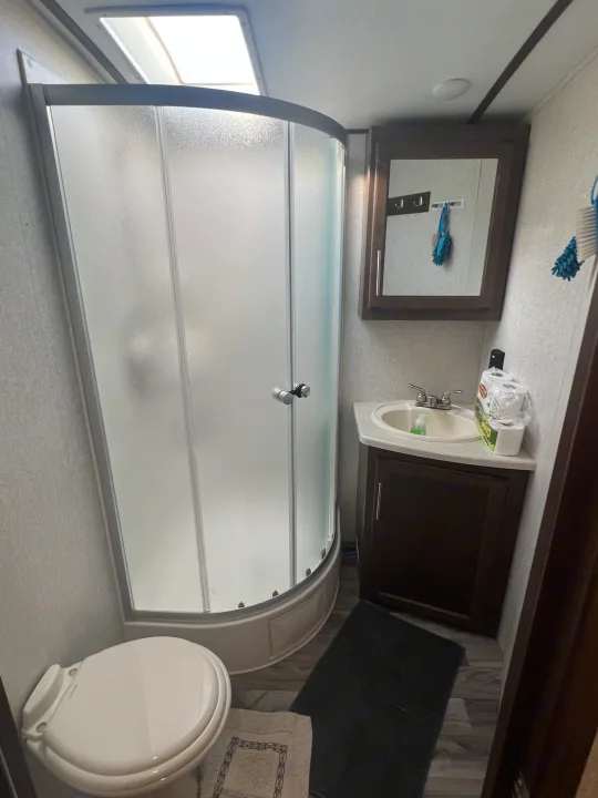 Inside an RV rental bathroom, featuring a curved shower, toilet, sink vanity, and overhead skylight for a bright, compact space.. Keystone RV Cougar 2019