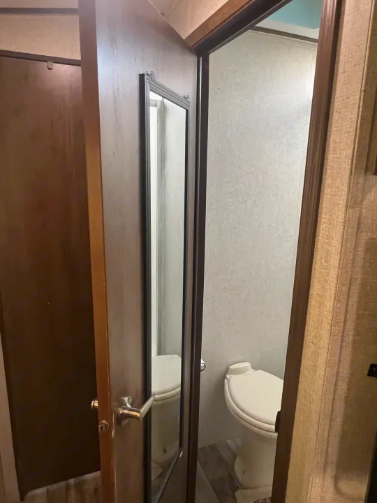 Inside an RV rental: a compact bathroom with a toilet and a door featuring a full-length mirror.. Keystone RV Cougar 2019