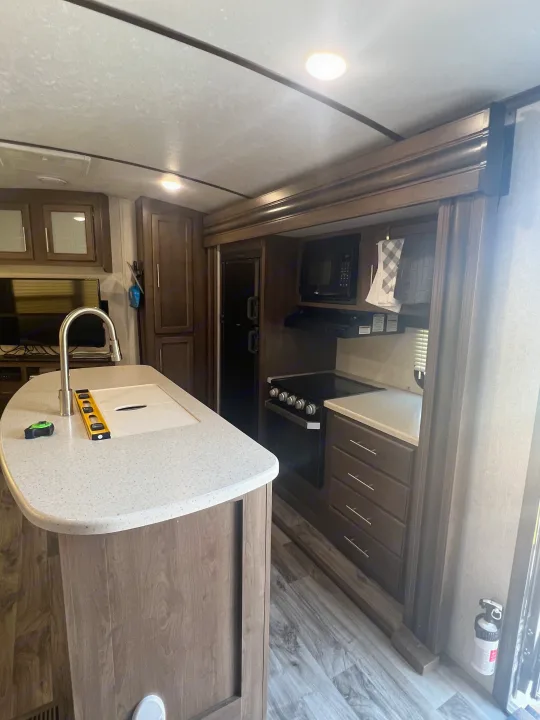 Modern RV rental kitchen with island, sink, stove, microwave, and refrigerator, offering practical amenities for travelers.. Keystone RV Cougar 2019