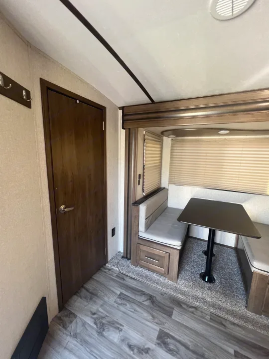 Inside an RV rental: a modern dinette with comfy benches, table, and storage. A door and coat rack are on the left wall.. Keystone RV Cougar 2019