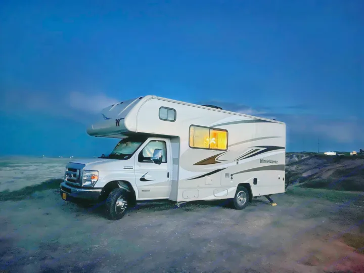 Night view of a white Minnie Winnie RV rental, interior lit up for camping, parked in a dark, open landscape.. Winnebago Minnie Winnie 2020