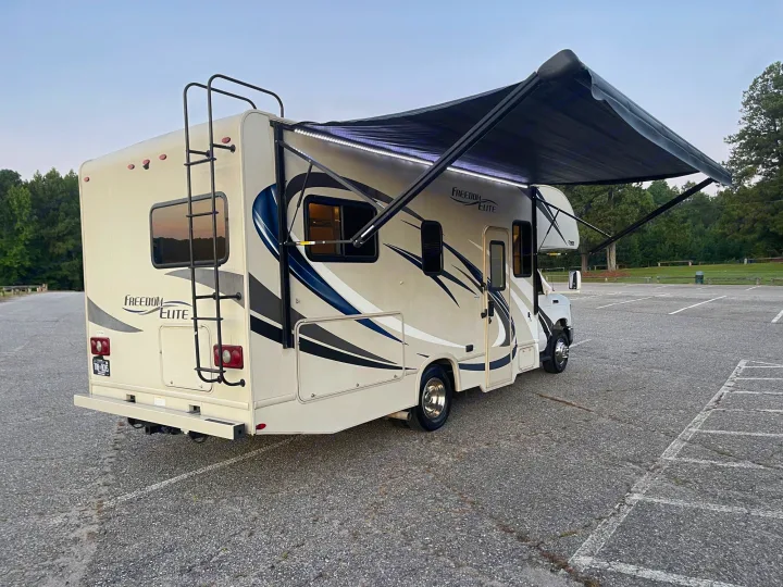 Spacious beige Freedom Elite RV rental in a parking lot at dusk, its lighted awning extended for adventure.. Thor Freedom Elite 2018