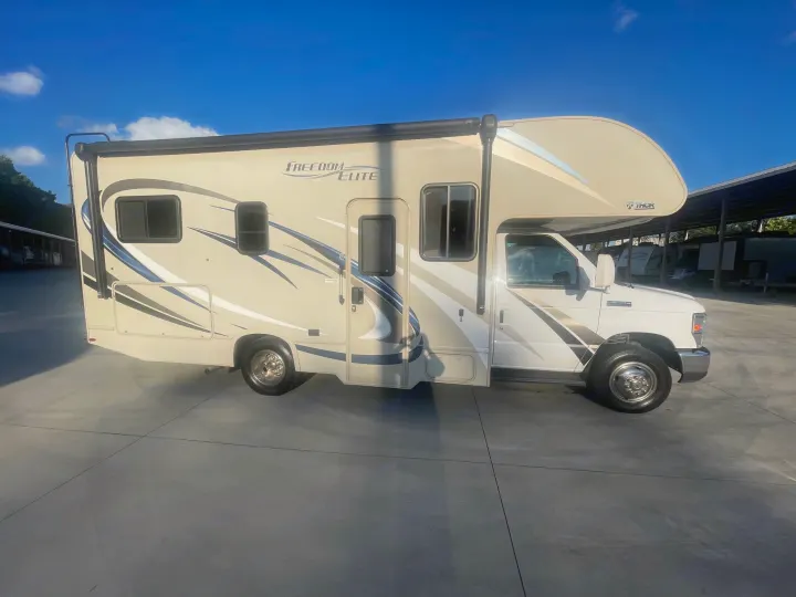 Beige and white Class C rv rental parked on concrete outdoors under a blue sky. Ready for your travel adventure!. Thor Freedom Elite 2018