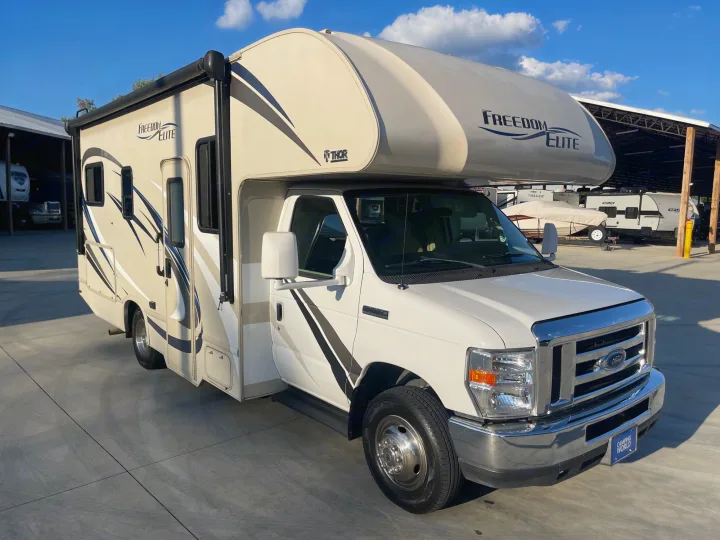 A beige Thor Freedom Elite Class C RV rental is parked outdoors on a sunny day, ready for adventure.. Thor Freedom Elite 2018