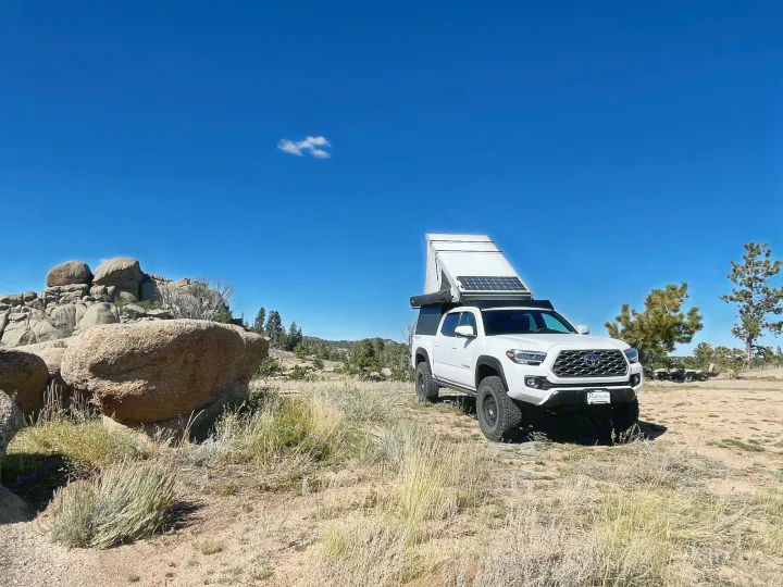 White Toyota Tacoma truck with pop-up camper & solar panels, ideal for an rv rental off-grid adventure.. 2023