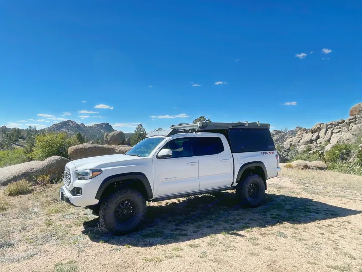 A white Toyota Tacoma with a truck bed camper parked in a scenic rocky landscape, ideal for an RV rental adventure.. 2023