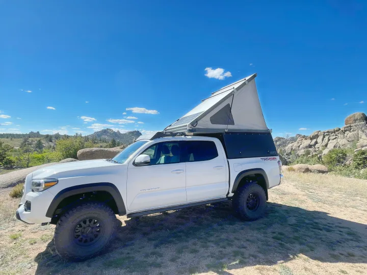 White Toyota Tacoma with a deployed pop-up camper, perfect for an RV rental adventure in rugged mountain scenery.. 2023