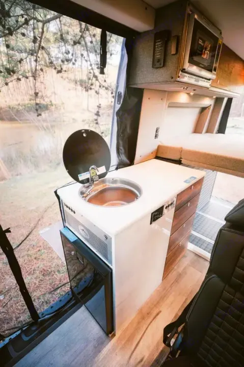 RV rental: Inside a camper van with a kitchenette (sink, fridge), microwave, and bed, next to a large window.. Storyteller Overland Storyteller Overland Class B 2022