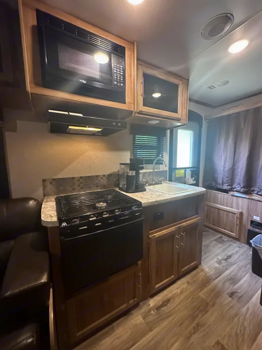 This RV rental kitchen is equipped with a microwave, stove, sink, and coffee maker, offering a compact and functional cooking area.. Jayco Jay Feather 2018