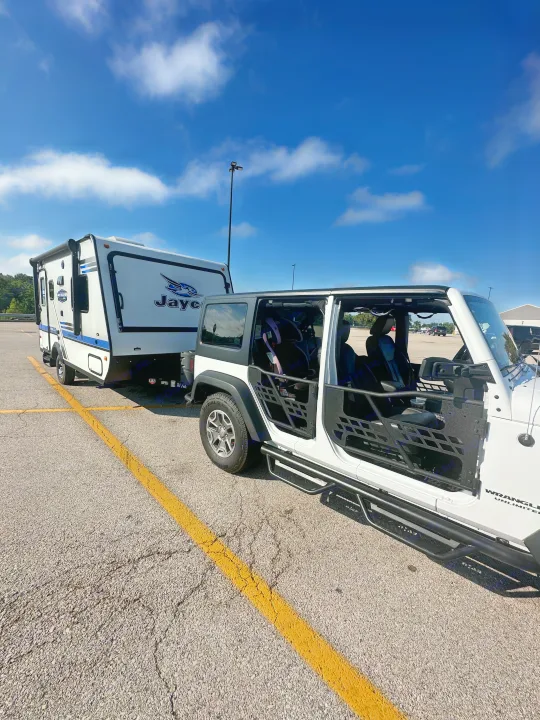 White Jeep pulling a Jayco travel trailer RV rental, set for a family camping road trip under blue skies.. Jayco Jay Feather 2018