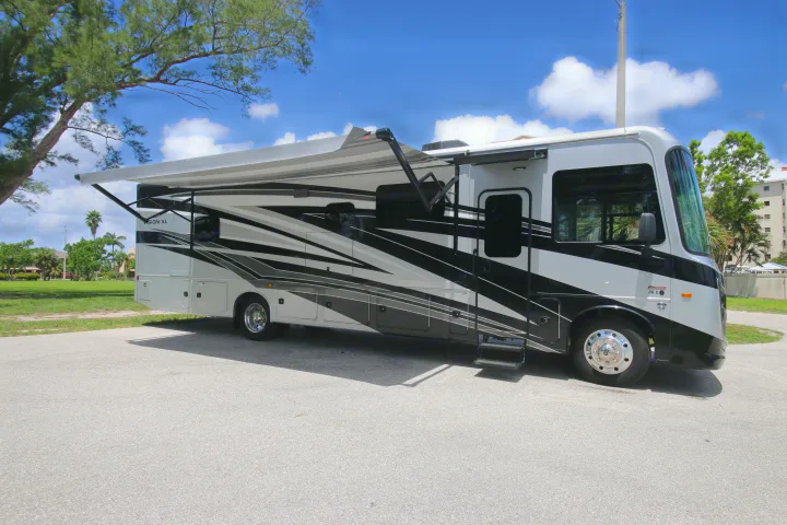 Modern gray and black RV rental, with awning extended, parked on asphalt under a sunny sky. Ready for adventure.. Entegra Coach Vision XL 2023