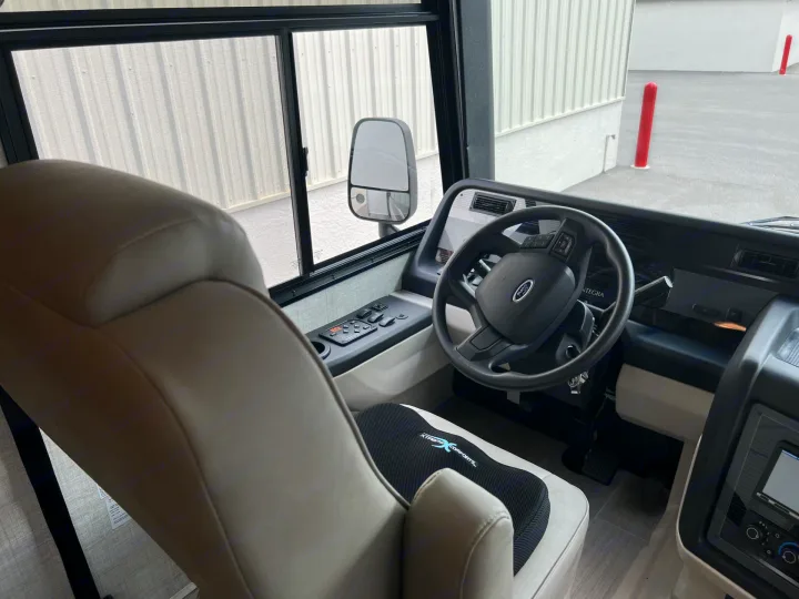 Driver's view from an RV rental, showing the Ford steering wheel, dashboard, and a comfort cushion on the spacious pilot seat.. Entegra Coach Vision XL 2023