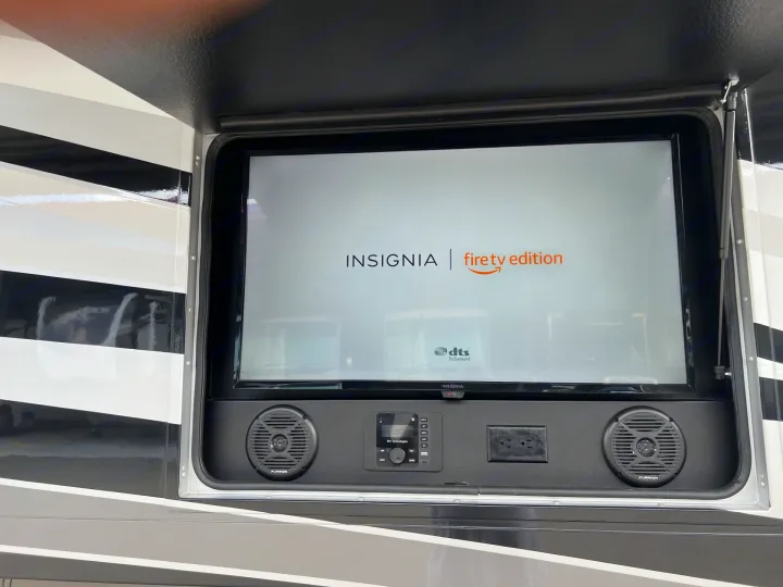 View of an RV rental's side bay, showcasing an Insignia Fire TV, Furrion speakers, and power outlet for outdoor entertainment.. Entegra Coach Vision XL 2023