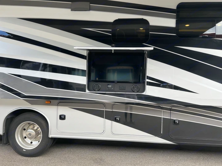Experience outdoor entertainment with this RV rental! Side view of a black, white, and gray motorhome with an open TV bay.. Entegra Coach Vision XL 2023