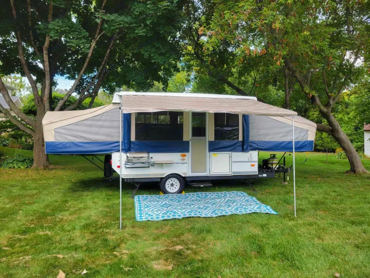 Pop-up RV rental deployed in a green yard. Canvas camper with awning & mat, ready for outdoor summer adventures.. Forest River Flagstaff M.A.C. 2011