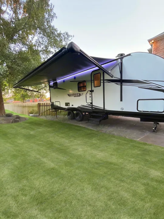 This RV rental, a white travel trailer with an extended awning and purple lights, is set up for outdoor leisure by a green lawn.. Forest River Tracer 2022