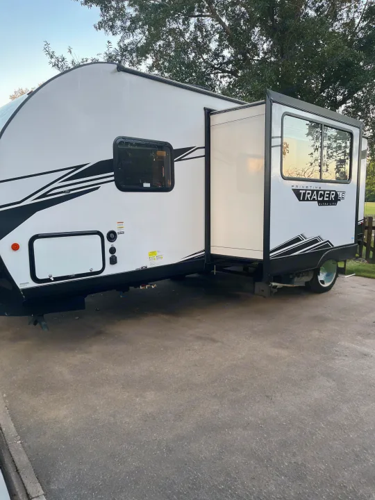 White travel trailer with extended slide-out. Explore the outdoors with this spacious RV rental.. Forest River Tracer 2022