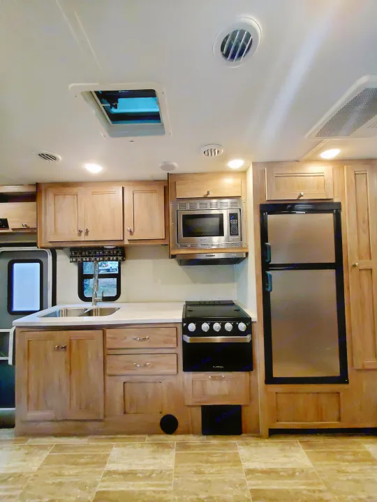 Well-designed RV rental kitchen: wood cabinets, double sink, microwave, stove, fridge, and overhead skylight.. Forest River Sunseeker 2019