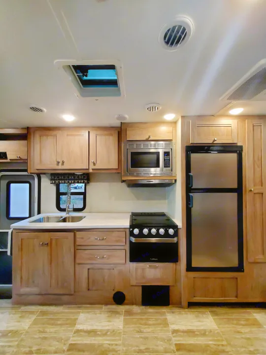 RV rental kitchen interior: bright with skylight, featuring wood cabinets, sink, microwave, range, and refrigerator.. Forest River Sunseeker 2019
