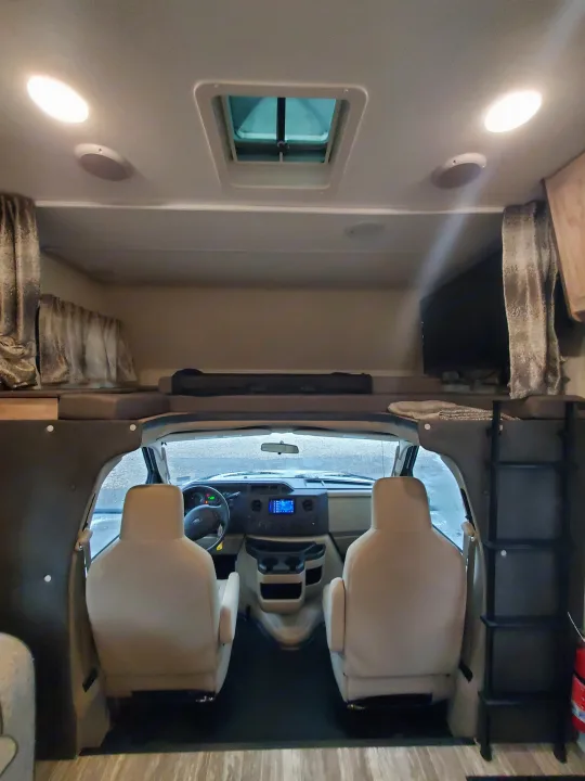 RV rental interior: View from the main cabin into the cockpit and spacious overhead sleeping bunk with TV.. Forest River Sunseeker 2019