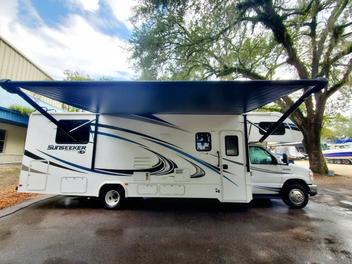 White Class C Sunseeker RV rental with its dark awning extended, parked on wet asphalt.. Forest River Sunseeker 2019