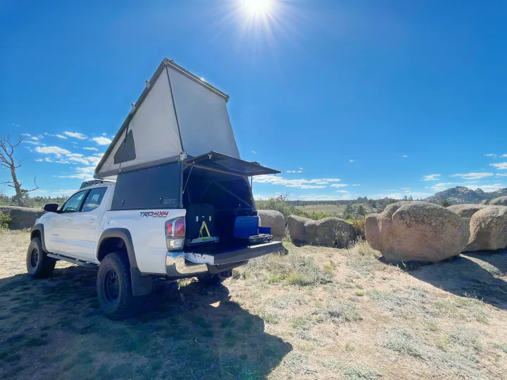 White Tacoma truck with pop-top camper, ready for an RV rental outdoor adventure in a scenic rocky landscape.. Toyota Tacoma TRD Off-Road 2023