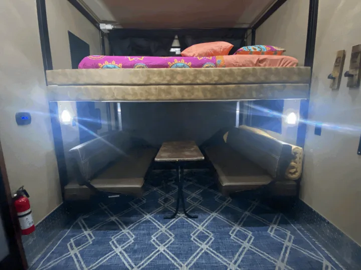 This RV rental features a functional interior: an elevated bunk bed, a compact dinette with table, and a blue patterned floor.. Forest River Vengeance 2015