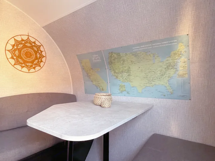 Inside an RV rental: a cozy dinette with bench seating, woven baskets, and a USA national parks map adorns the wall.. Braxton Creek Bushwhacker Plus 2022
