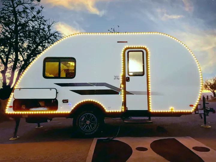 This RV rental shines brightly with warm lights outlining its shape against a beautiful sunset sky, ideal for an evening getaway.. Braxton Creek Bushwhacker Plus 2022