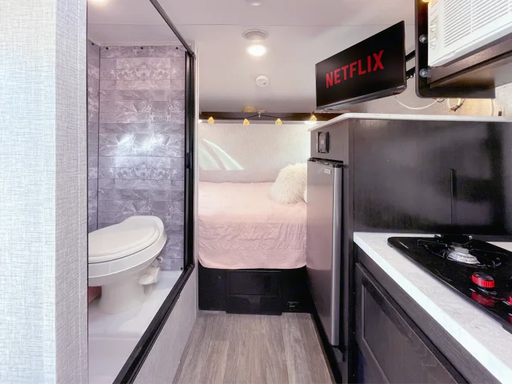 An inviting RV rental interior featuring a compact bath, cozy bedroom, kitchenette, and Netflix TV.. Braxton Creek Bushwhacker Plus 2022