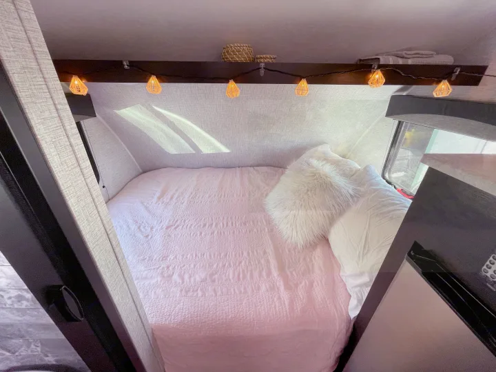 Inviting RV rental bedroom: cozy pink bed, fluffy pillows, and warm string lights create a perfect retreat.. Braxton Creek Bushwhacker Plus 2022