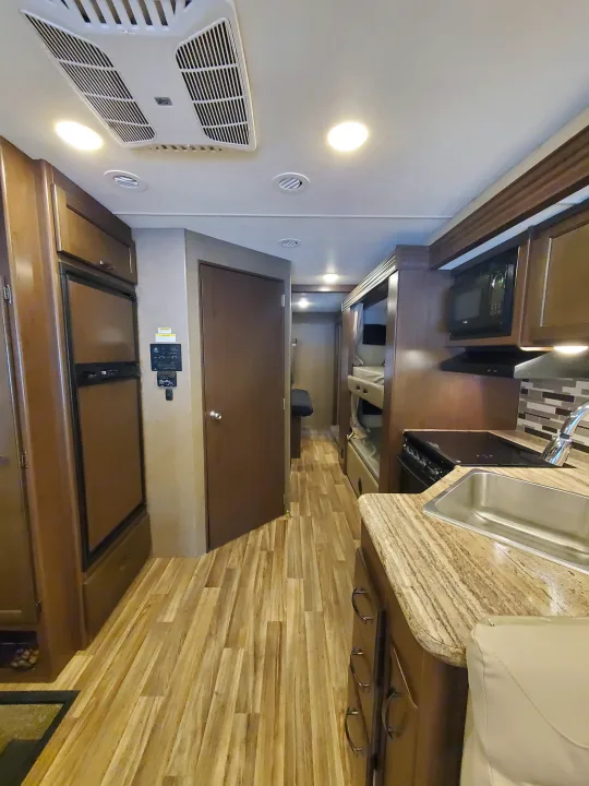 Bright rv rental interior showing kitchen with sink, stove, microwave, fridge, and a hallway leading to bunk beds.. Thor Motor Coach A.C.E 2018