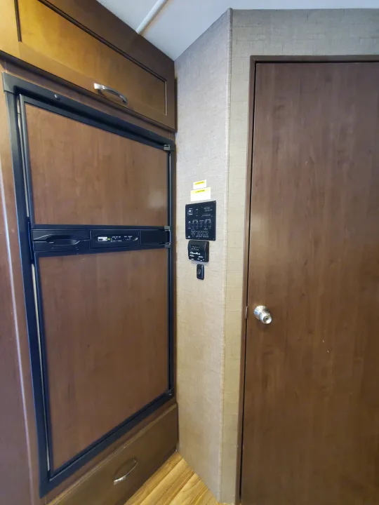 RV rental interior: wood-paneled refrigerator, Thor Motor Coach control panel, cabinet, and an interior door.. Thor Motor Coach A.C.E 2018
