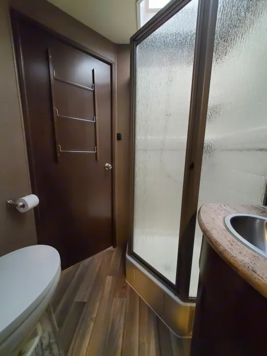 This RV rental features a compact bathroom with a toilet, shower with frosted glass, and a small sink on a wood-look floor.. Thor Motor Coach A.C.E 2018