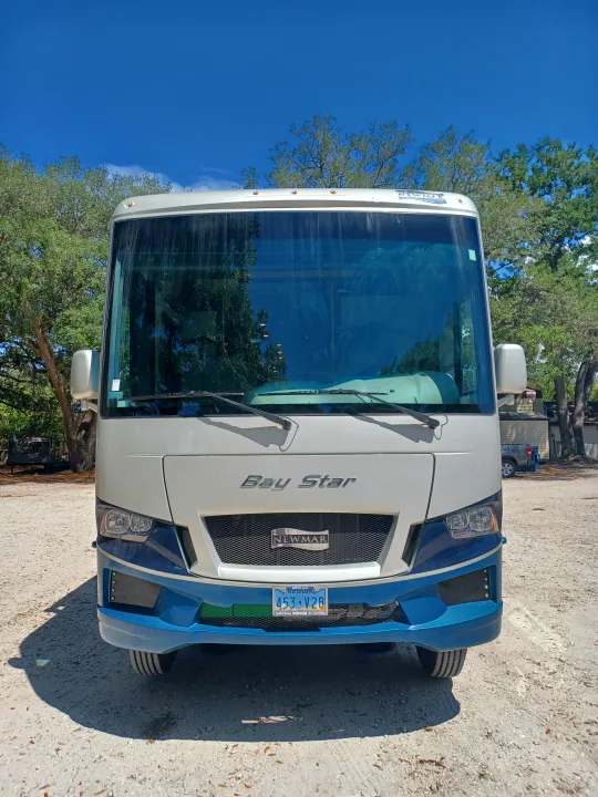 Front view of a white and blue Newmar Bay Star motorhome, parked on a gravel lot. Consider this spacious RV for your next rv rental adventure.. Newmar Bay star 2022