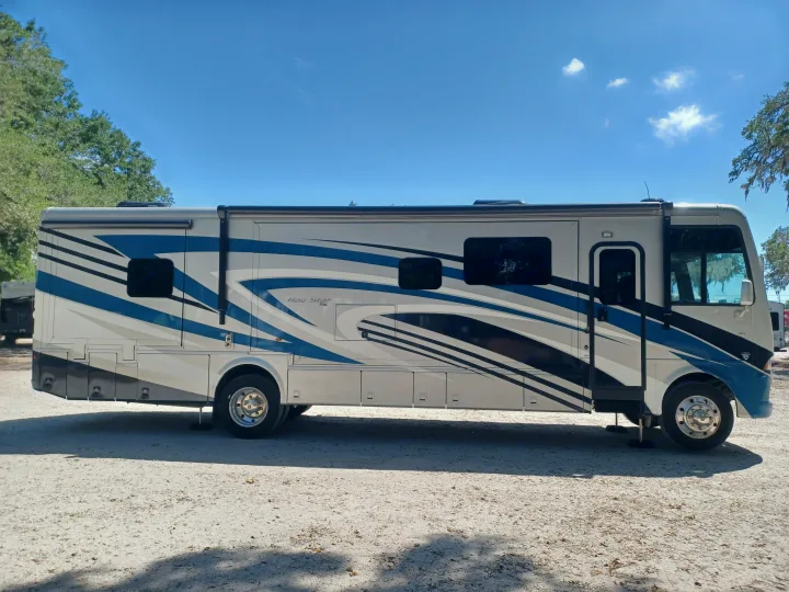 Full side view of a large, modern Bay Star RV rental, grey with striking blue/black stripes, parked on a sandy lot.. Newmar Bay star 2022
