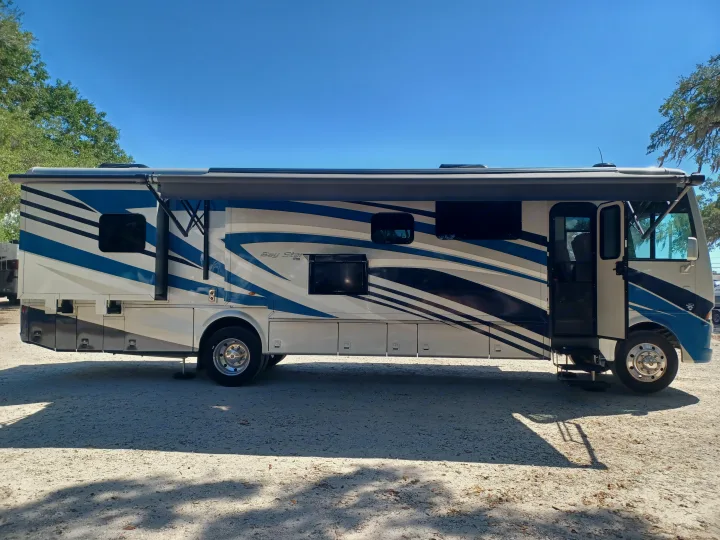 Bright blue and white Newmar Bay Star RV, door open and awning extended, parked on gravel. Perfect for your next rv rental adventure!. Newmar Bay star 2022