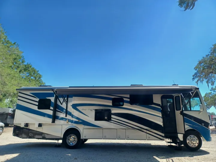 A white, blue, and black Bay Star RV rental with an extended awning, parked outdoors under a clear sky. The door is open.. Newmar Bay star 2022