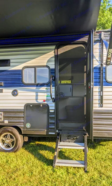 Side view of an RV rental with its entry door open, showing extended steps and a blue-lit awning. Parked on grass.. Cherokee wolf pup 2021