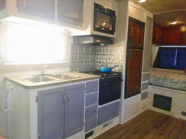 Modern RV rental interior: a clean kitchen with gray cabinets, sink, and stove, extending to a cozy bed area.. Fleetwood Jamboree 2009