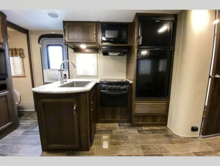 RV rental kitchen: Features dark wood cabinets, a sink, black stove, microwave, and tall black refrigerator. Ready for trips.. Keystone RV Bullet Ultra Lite 2018