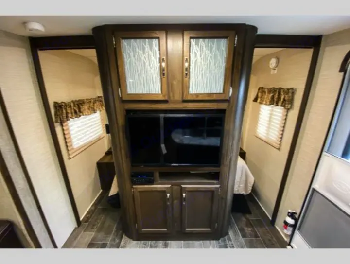 RV rental interior: A compact living space featuring a central entertainment unit with TV, flanked by two cozy bedrooms with windows.. Keystone RV Bullet Ultra Lite 2018