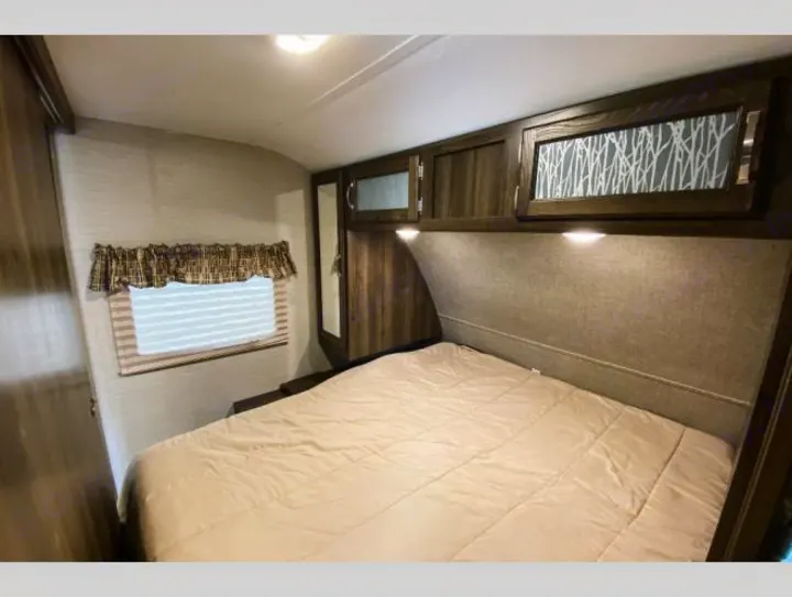 Cozy RV rental bedroom featuring a comfortable bed, overhead cabinets with lights, and a window for natural light.. Keystone RV Bullet Ultra Lite 2018