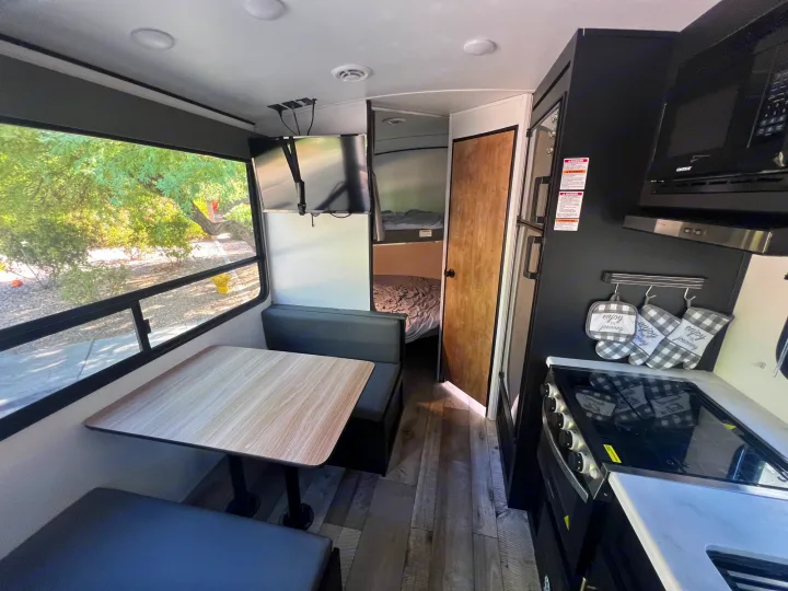 RV rental interior: dining booth, kitchen with stove/microwave, and a cozy sleeping area, all in a modern design.. Keystone RV Springdale 2022