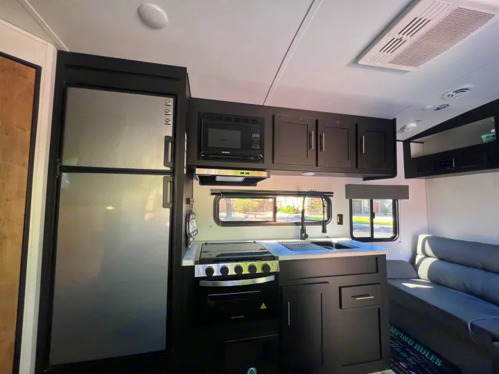 Spacious RV rental kitchen with modern black cabinets, stainless steel fridge, microwave, stove, and a comfy dinette.. Keystone RV Springdale 2022