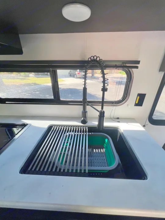 Inside an rv rental, a sleek kitchen features a black sink, modern faucet, and white countertop with a drying rack.. Keystone RV Springdale 2022