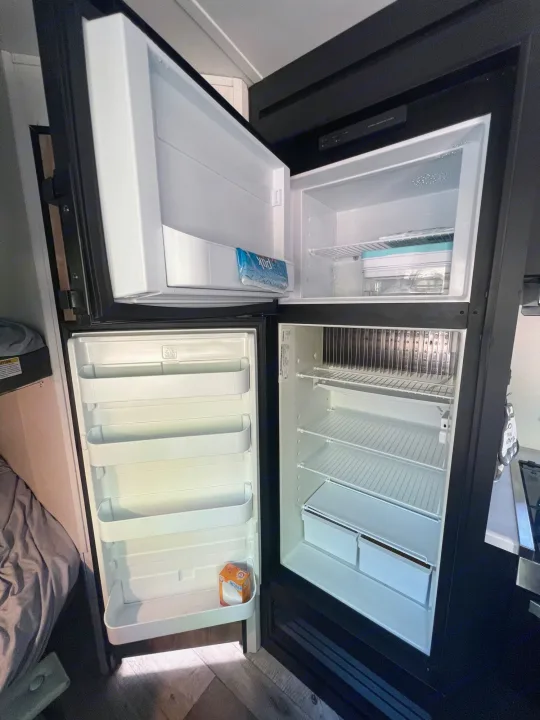 Open RV rental fridge and freezer, ready for your camping kitchen. White interior with shelves, crispers, and baking soda.. Keystone RV Springdale 2022
