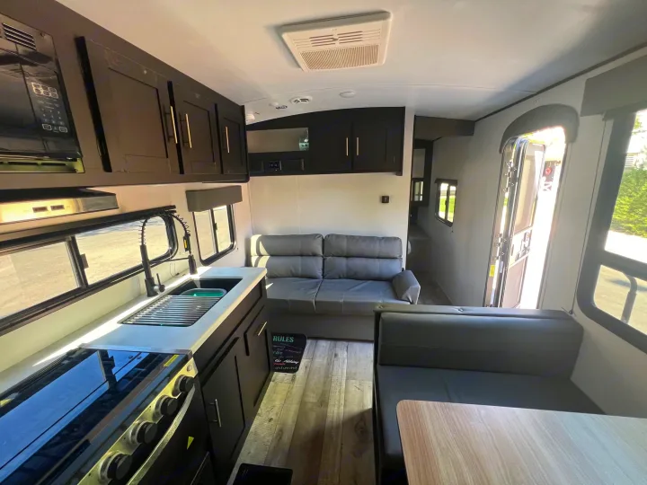 Modern RV rental interior with a fully equipped kitchen (stove, sink) and a cozy living area featuring a sofa and dinette.. Keystone RV Springdale 2022
